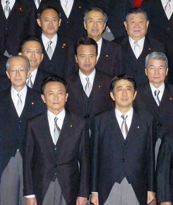 2006 में प्रधान मंत्री शिंजो आबे के पहले प्रशासन के तहत नव नियुक्त कैबिनेट मंत्रियों के लिए एक फोटो सत्र के दौरान योशीहिदे सुगा (पीछे की पंक्ति, बहुत बाईं ओर)