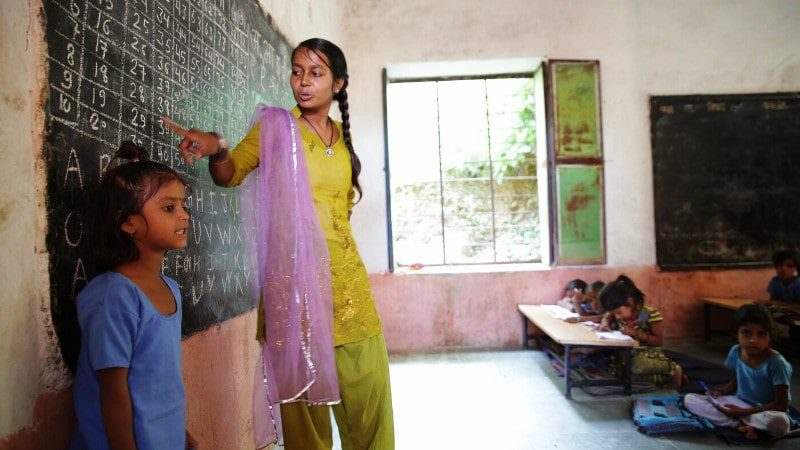 एक शिक्षित बालिका स्वयंसेवक ग्रामीण शहर के एक स्कूल में पढ़ाती है
